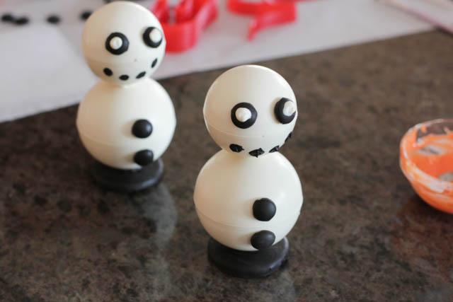 Assembling the chocolate snowmen -Attach the eyes to the snowman using a bit of melted chocolate. Then, make four dots for the mouth using a brush and black melted chocolate. 