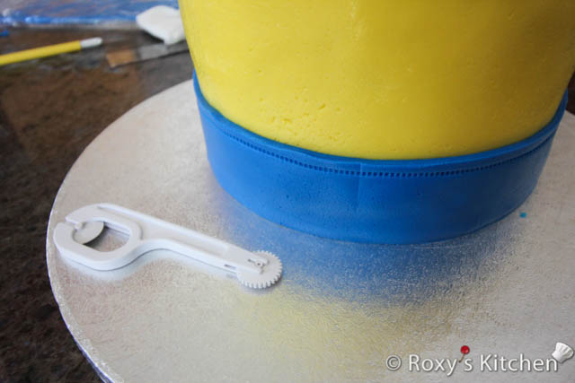 Brush some water at the base of the minion cake and place the blue fondant on top. 