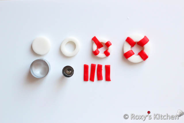 Cut four thin strips out of the rolled red fondant using the X-Acto knife and use water to attach them around your life ring as seen in the picture below. 