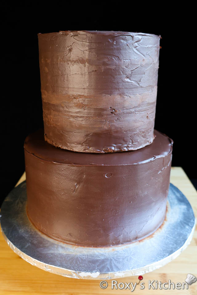Stacking a two-tier cake covered in chocolate ganache. 