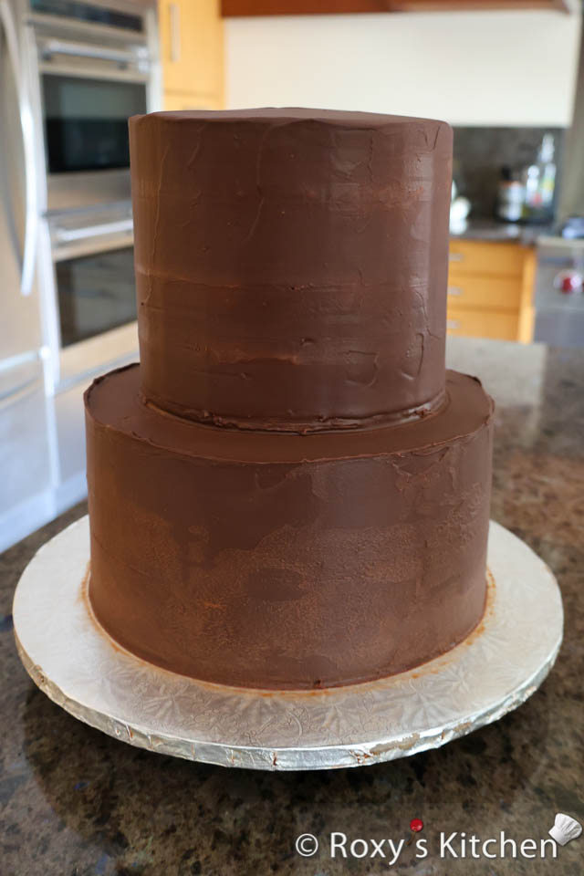 Lastly, apply a thicker layer of semi-sweet chocolate ganache on the two tier cake and smooth it out using a spatula and a cake scraper / smoother. Use an offset spatula to smooth the top and use a cake scraper to smooth the sides. 
