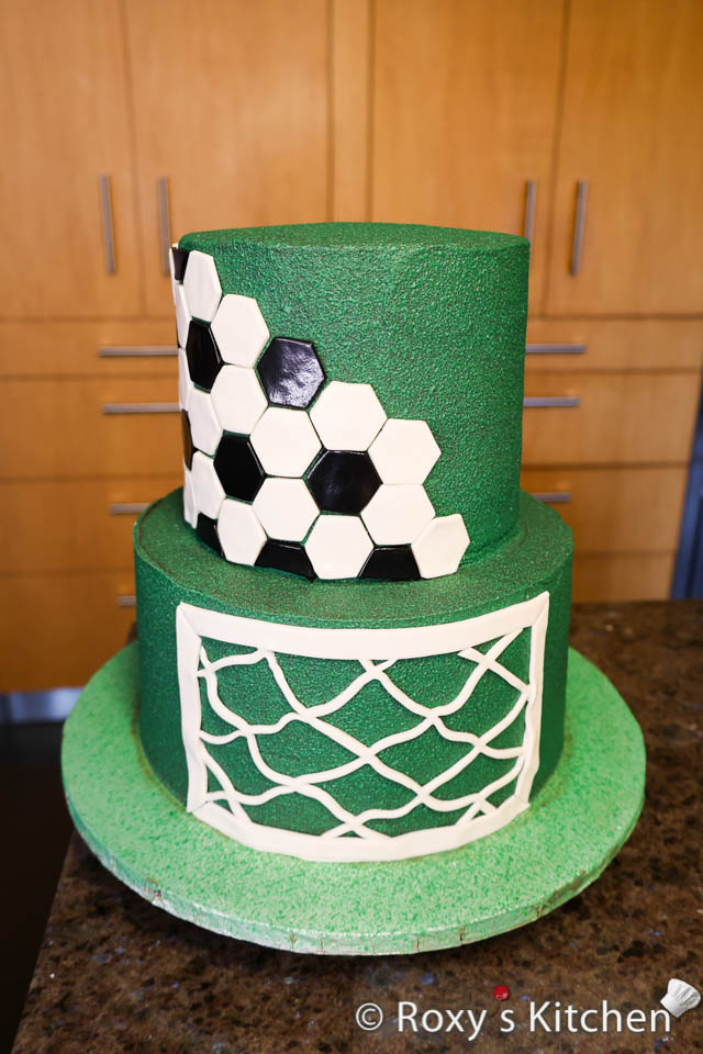 Carefully lift the soccer net with both hands and attach it to the front of the bottom cake tier. You might need to brush a bit of water on the back of the net so that it sticks to the cake better. 